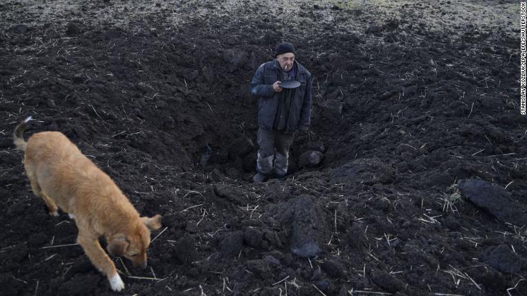 ウクライナ・タマルチュクで自宅裏の畑への砲撃であいた穴の大きさを示す男性＝２０日/Stanislav Kozliuk/EPA-EFE/Shutterstock
