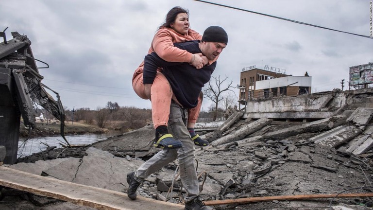 キエフ近郊の街イルピンで、女性を背負って避難する男性/Oleksandr Ratushniak/AP
