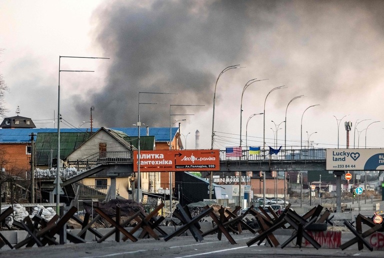 障害物が置かれた道路の向こうで煙が立ち上るキエフの街/Fadel Senna/AFP/Getty Images