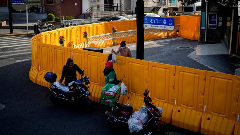 封鎖区域で障壁越しに食料品を渡す配達員＝２３日、上海/ALY SONG/REUTERS