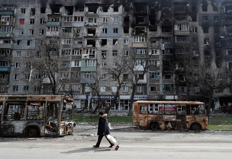 焼け焦げたバスの横を歩く住民＝１９日、ウクライナ・マリウポリ/Alexander Ermochenko/Reuters