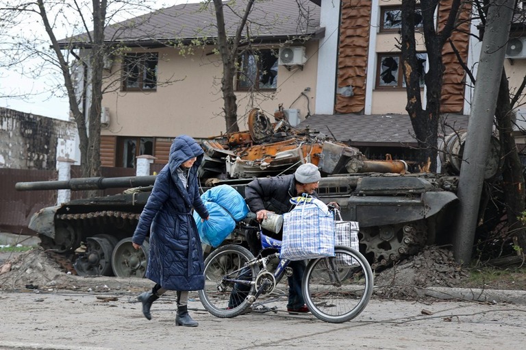 マリウポリで激しい戦いが続く中、破壊された戦車の横を通り過ぎる市民＝１９日/Alexei Alexandrov/AP