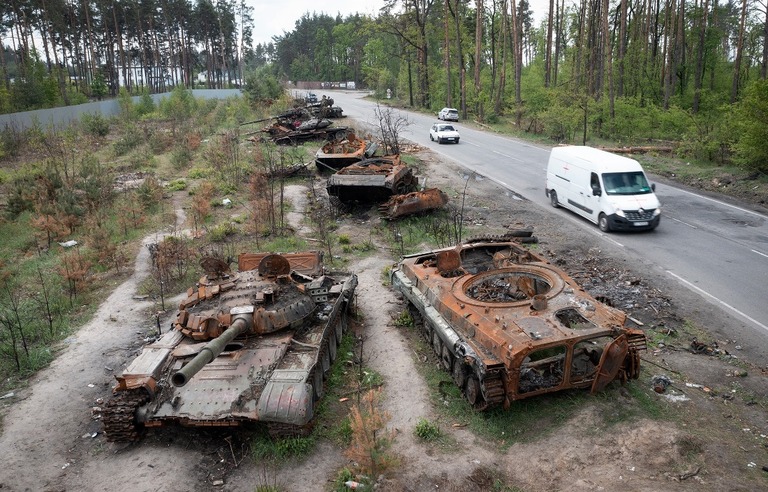 ウクライナでの戦闘で破壊されたロシア軍の戦車の脇を乗用車が通過する/Efrem Lukatsky/AP