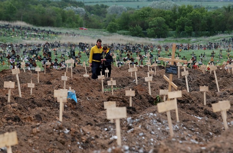 新しく作られた墓の前に立つ人＝２２日、ウクライナ・パリウポリ郊外/Alexander Ermochenko/Reuters