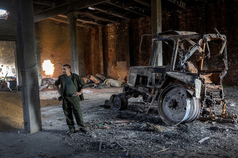ロシア軍の戦車の砲撃で破壊されたトラクターのそばに立つウクライナの農業従事者/John Moore/Getty Images