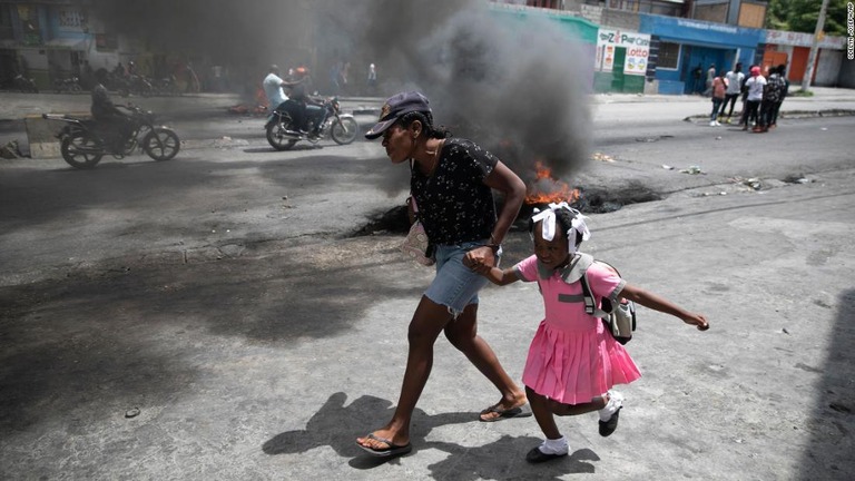 ハイチ首都での暴力増加に対する抗議デモの最中、火の手から逃げる女性と子ども/Odelyn Joseph/AP