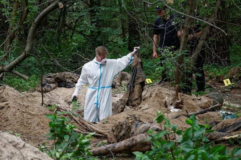 集団墓地とされる場所を調べる係官＝１３日、ウクライナ・キーウ（キエフ）州/Valentyn Ogirenko/Reuters
