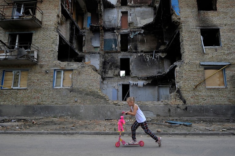 破壊された住宅棟の前をキックスクーターで走り過ぎる少女/Sergei Chuzavkov/AFP/Getty Images