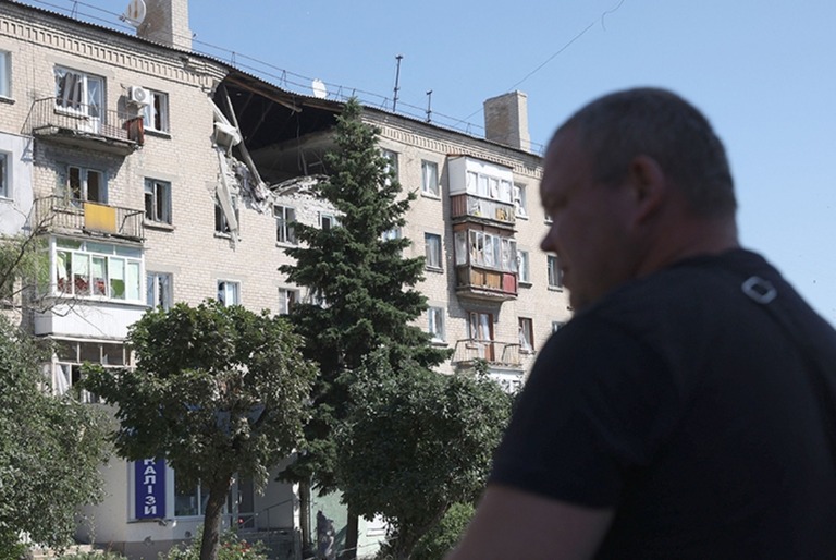 リシチャンスクの街路で損壊した居住施設の前を歩く男性/Anatolii Stepanov/AFP/Getty Images