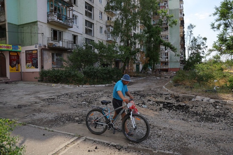 自転車を押しながらセベロドネツクの建物の前を歩く住人＝７月１日撮影/Victor/Xinhua/Getty Images
