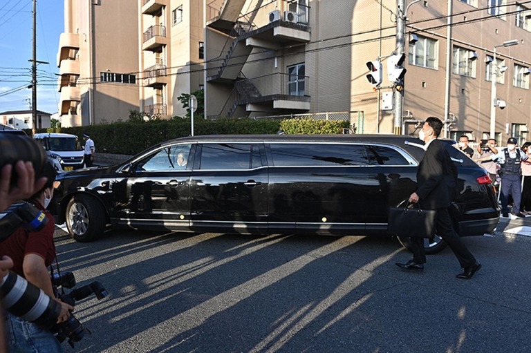 安部氏の遺体を乗せているとみられる車が、奈良県立医科大学附属病院前にいる警官や報道陣の間を通り過ぎる様子＝９日/Philip Fong/AFP/Getty Images