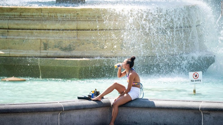 噴水の前で水分を摂取する女性＝１９日、英ロンドンのトラファルガー広場/Dominic Lipinski/AP