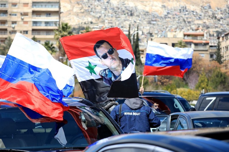 シリア首都ダマスカスで開かれたロシア支持の集会でロシア国旗とシリアのアサド大統領が描かれた旗を振るシリア国民＝３月２５日/Louai Beshara/AFP/Getty Images