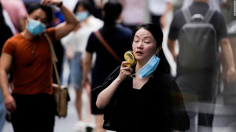 歩きながら携帯扇風機を使用する女性＝１９日、上海市/Aly Song/Reuters