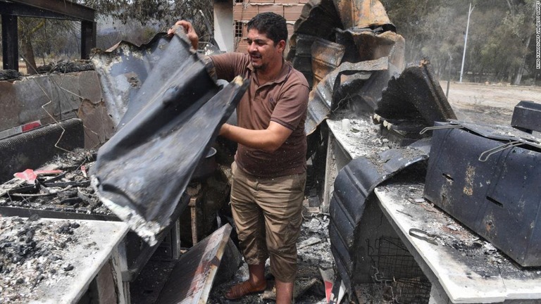 火災の後、焼け焦げた物をみる男性＝１７日、アルジェリアのエルカラ市/RYAD KRAMDI/AFP via Getty Images