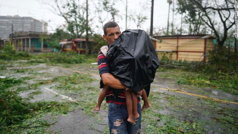 雨の中、子どもを運ぶ男性＝２７日、キューバのピナール・デル・リオ/Alexandre Meneghini/Reuters