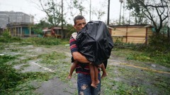 雨の中、子どもを運ぶ男性＝２７日、キューバのピナール・デル・リオ