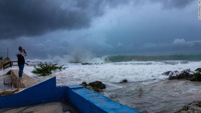 波が護岸に打ち寄せる様子を撮影する女性＝２６日、ケイマン諸島・ジョージタウン/Kevin Morales/AP