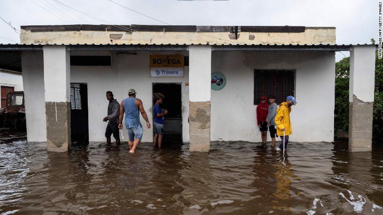浸水した倉庫の外に立つ人々＝２７日、キューバ・バタバノ/Yamil Lage/AFP/Getty Images