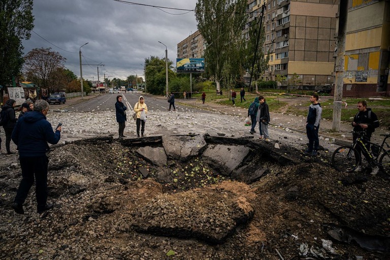 ロシア軍によるミサイル攻撃後に陥没した道路を眺める地元住民ら＝１０日、ウクライナ・ドニプロ/Dimitar Dilkoff/AFP/Getty Images