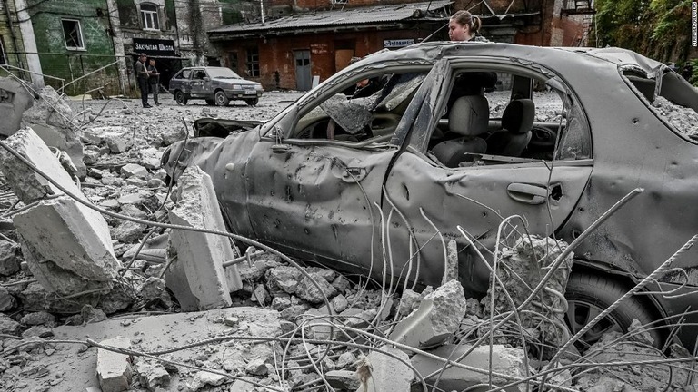 ロシアのミサイル攻撃で破壊された車両のそばに立つ女性＝ザポリージャ、１４日撮影/Stringer/Reuters