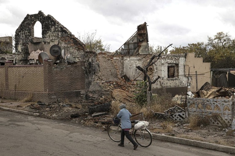 ヘルソン州で壊れた建物の前を歩く女性＝２４日/Metin Aktas/Anadolu Agency/Getty Images