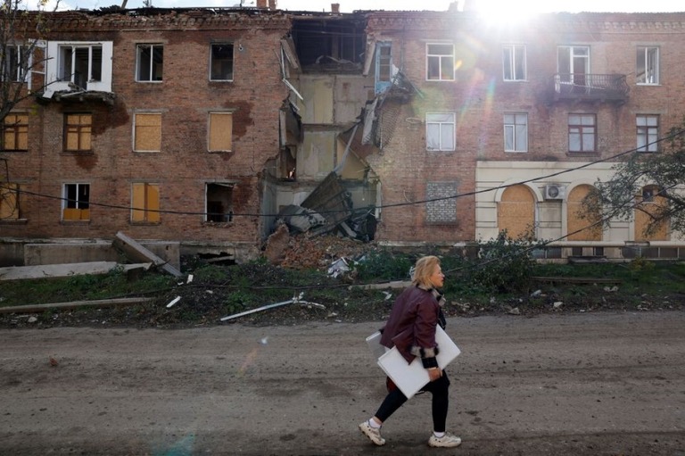 ミサイル攻撃で被害を受けた建物の前を歩く女性＝１日、ウクライナ東部ドネツク州バフムート/Clodagh Kilcoyne/Reuters
