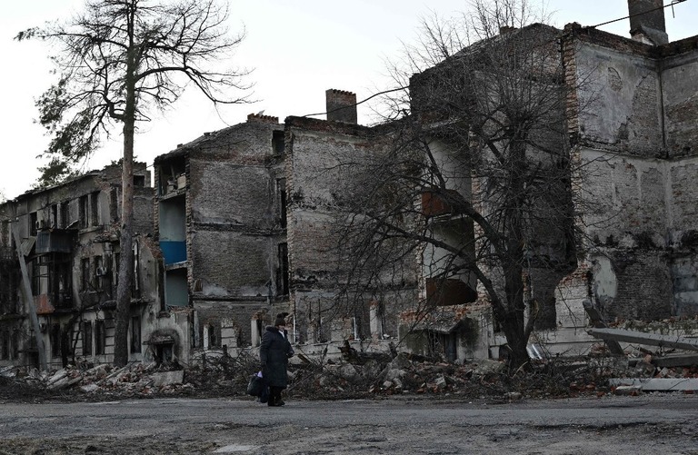 ウクライナ東部ドネツク州リマンで、破壊された建物の前を歩く人/Genya Savilov/AFP via Getty Images