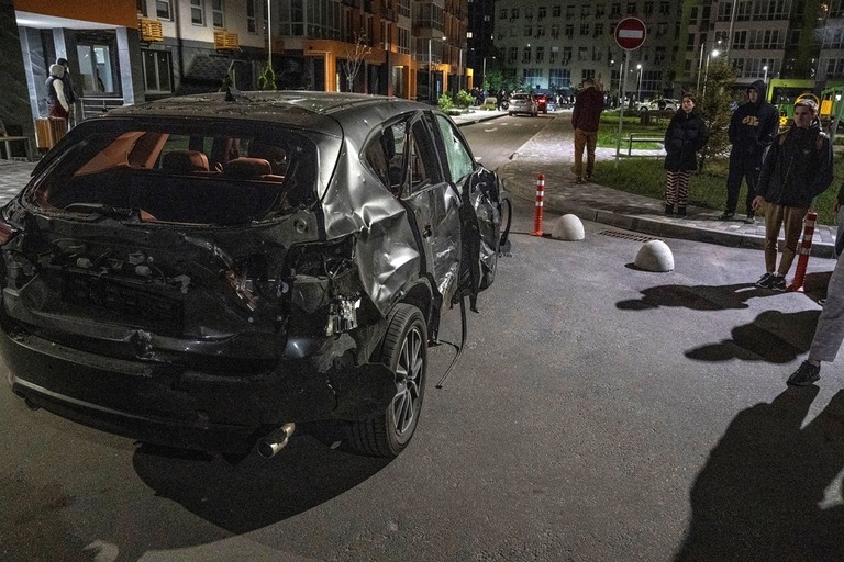 キーウを攻撃したドローンが撃墜された後、損傷した車両の近くに立つ住民ら/Oleksandr Khomenko/Reuters