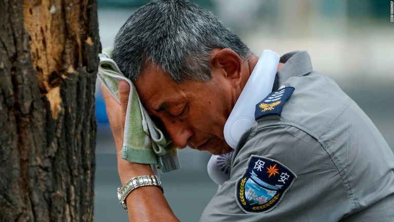 扇風機を首に掛けて汗を拭う警備員＝３日、中国・北京/Andy Wong/AP