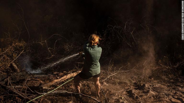 山火事に見舞われた場所へホースで水を撒く女性＝８月１４日/Bryan Anselm/The New York Times/Redux