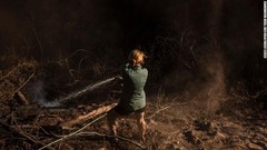山火事に見舞われた場所へホースで水を撒く女性＝８月１４日