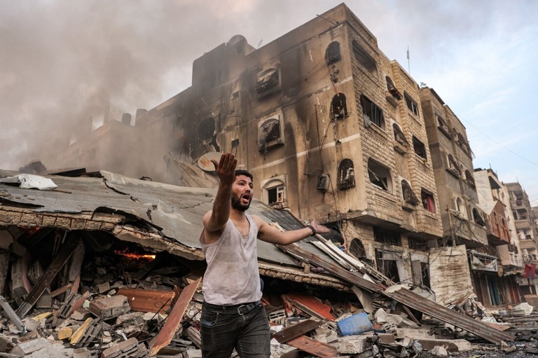 火の手が上がる倒壊した建物の前で叫ぶ男性＝１１日、ガザ市/Mohammed Abed/AFP/Getty Images