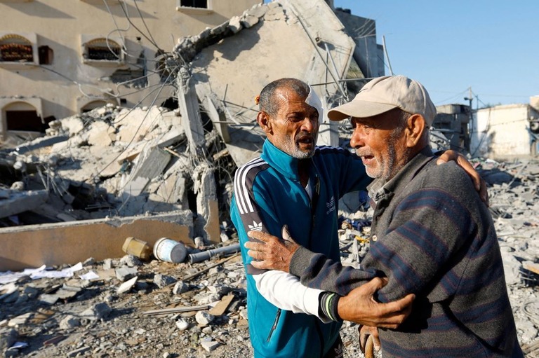 イスラエル軍による攻撃を受けて倒壊した住宅前に立つパレスチナ人ら＝１５日、パレスチナ自治区ガザ地区南部ハンユニス/Ibraheem Abu Mustafa/Reuters