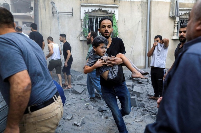 イスラエル軍の攻撃により負傷した子どもを運ぶ男性＝１９日、ガザ地区南部ハンユニス/Yasser Qudih/Reuters