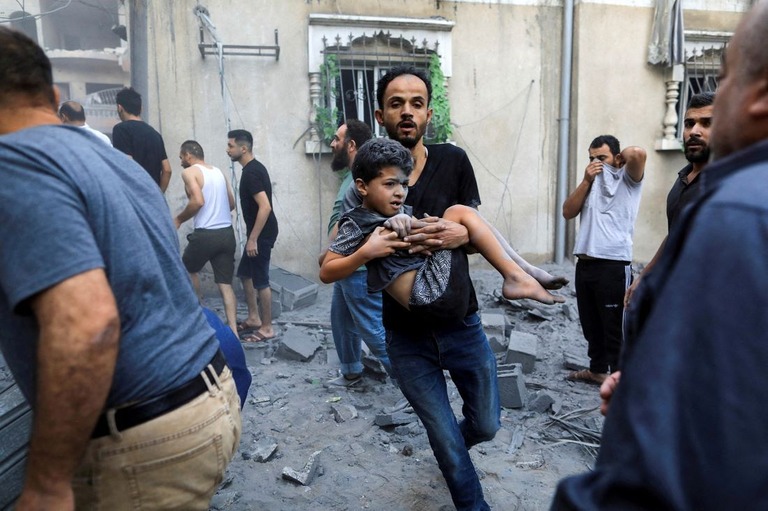 イスラエル軍の攻撃により負傷した子どもを運ぶ男性＝１９日、ガザ地区南部ハンユニス/Yasser Qudih/Reuters