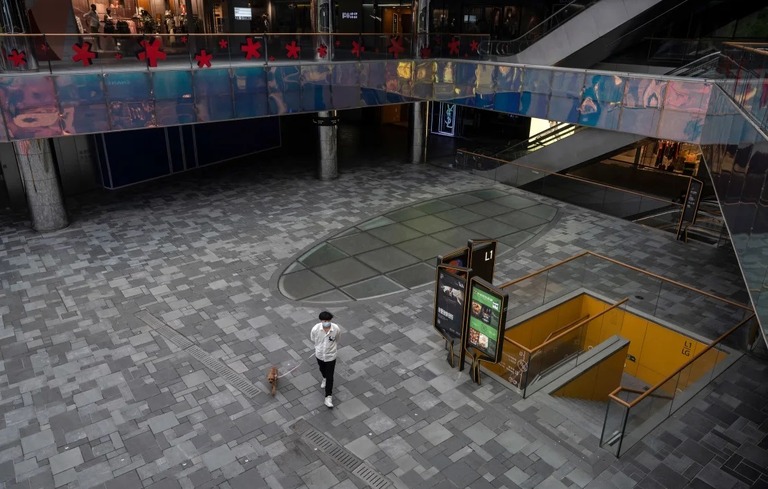 新型コロナ対策のロックダウン（都市封鎖）によって閉鎖されたショッピングモールを犬を連れて歩く男性＝２０２２年/Kevin Frayer/Getty Images