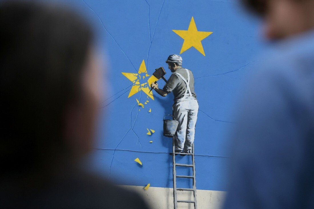 英国のグラフィティアーティスト、バンクシーの壁画の近くに立つ人々。壁画は欧州連合（ＥＵ）をテーマにした旗の星の一つを削る職人を描いている＝２０１７年