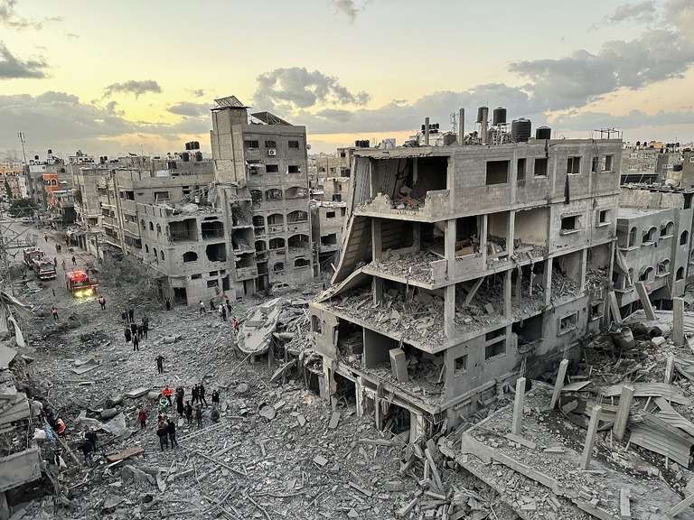 イスラエル軍の攻撃によって破壊された建物の間を歩くパレスチナ人＝２１日、パレスチナ自治区ガザ地区ジャバリヤ/Abed Sabah/Reuters