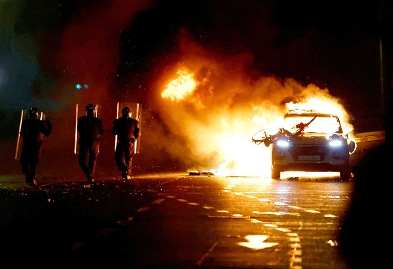 暴動が発生した現場近くで炎上する警察車両と機動隊＝アイルランド・ダブリン/Clodagh Kilcoyne/Reuters