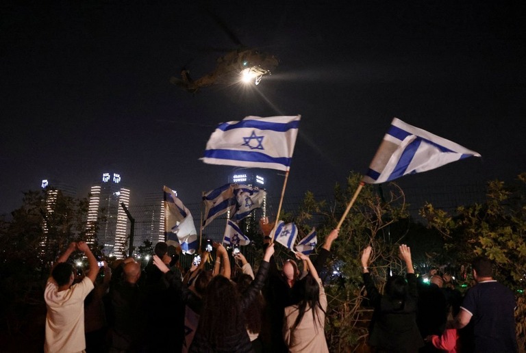 イスラエル国旗を振り、人質を乗せたヘリコプターの到着を歓迎する人々/Ronen Zvulun/Reuters
