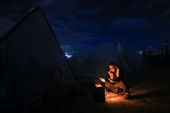 家を追われ避難先のテントで暖を取る男性＝１１月２７日、パレスチナ自治区ガザ地区ハンユニス