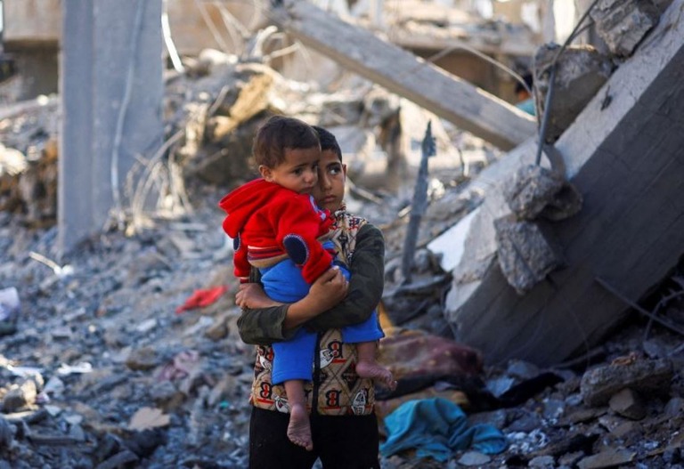 ガザ南部ラファの破壊された建物のそばで赤ちゃんを抱いて立つパレスチナ人の少年/Mohammed Salem/Reuters