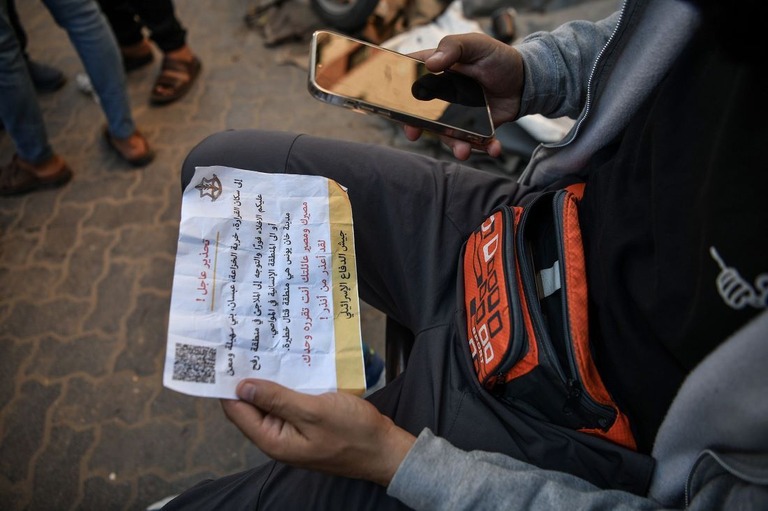 イスラエル軍が投下したＱＲコード付きのビラを手にするパレスチナ人/Abed Zagout/Anadolu/Getty Images