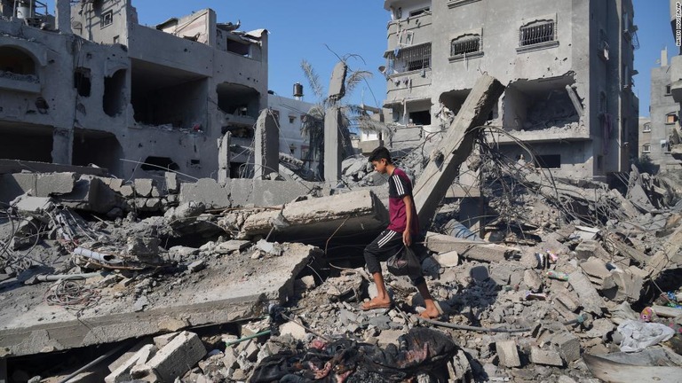 ガザ地区中部デイルアルバラの瓦礫の中を歩く男性/Hatem Moussa/AP