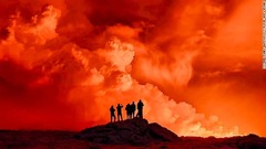 溶岩が夜空をオレンジ色に染める中、立ち上る煙を眺める地元住民