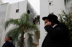 ロケット弾で損傷した建物の近くを歩く人々＝１２月５日、イスラエル・アシュケロン