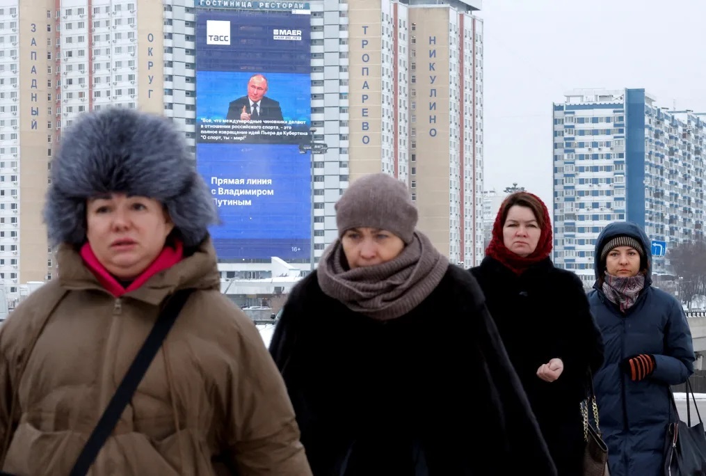 モスクワ市内で女性たちが歩く背後の電光掲示板に、プーチン大統領の会見の様子が映る/Maxim Shemetov/Reuters