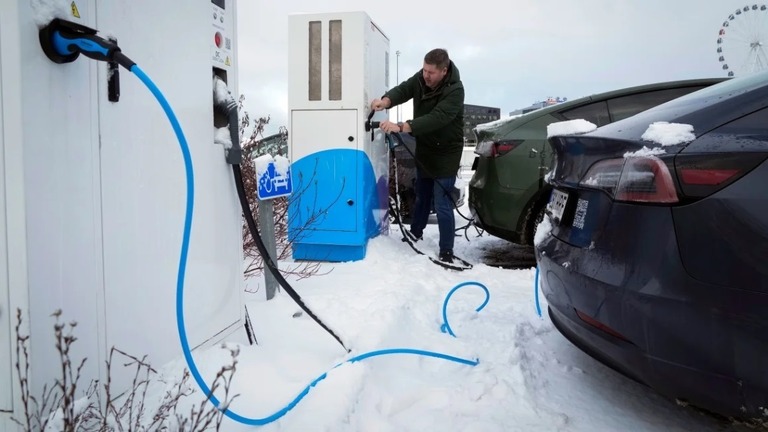 ショッピングモールの駐車場で電気自動車の充電を行う男性＝２０２３年２月、エストニア・タリン/Sergei Grits/AP