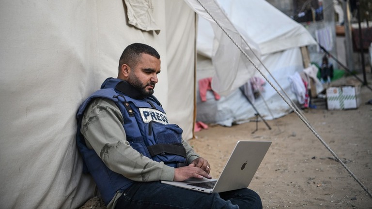 ガザ地区のラファでテントの横に座り、インターネット接続を試みる報道関係者/Abed Zagout/Anadolu/Getty Images